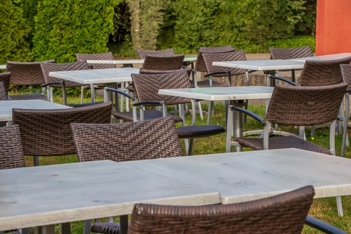 Geflochtene Stühle und helle Tische vor der Hecke
