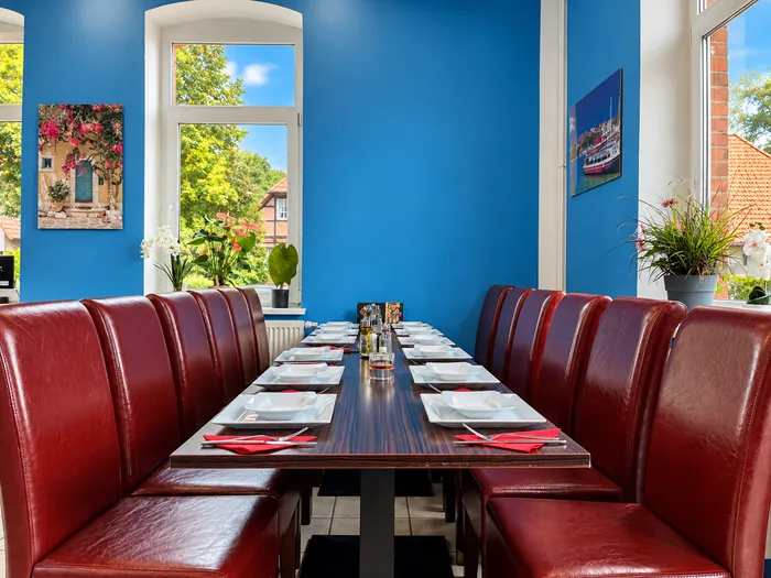 Lange Tafel für Gruppen mit roten Lederstühlen zwischen zwei Fenstern