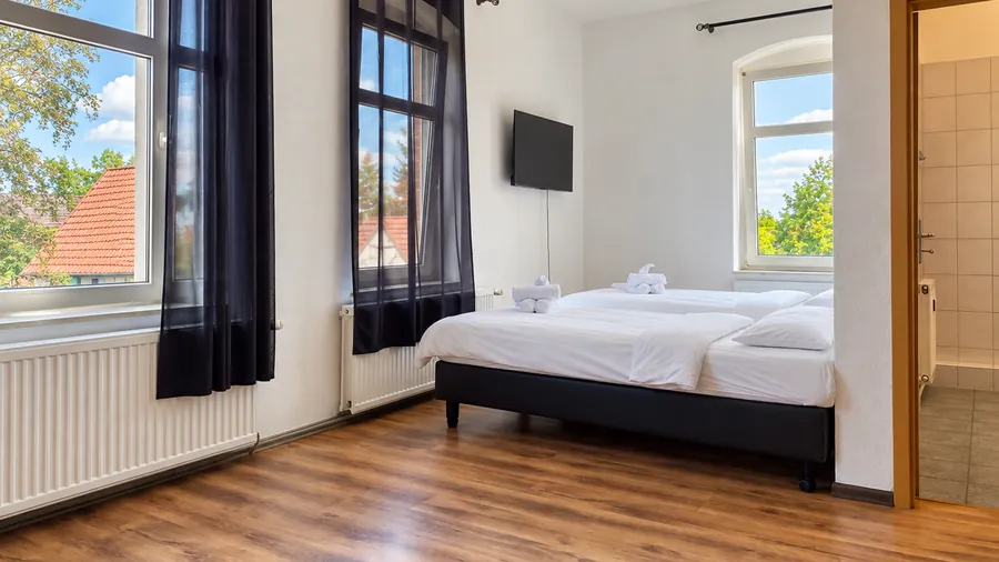 Helles Gästezimmer mit hohen Fenstern, Holzboden und frisch bezogenen Betten