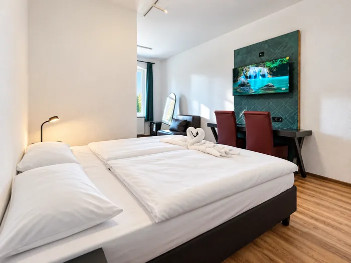 Doppelbett vor der dunkelgrünen Wand mit Fernseher und Schreibtisch