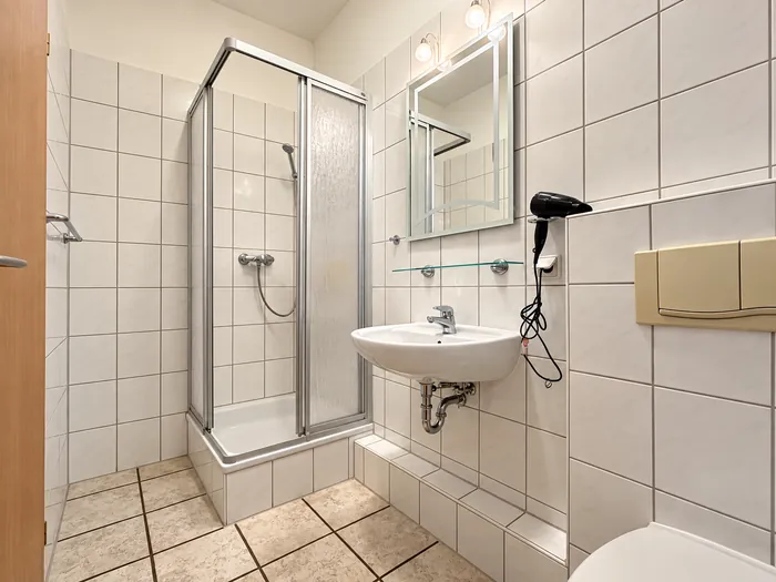 Bad mit Dusche, Waschbecken und beleuchtetem Spiegel