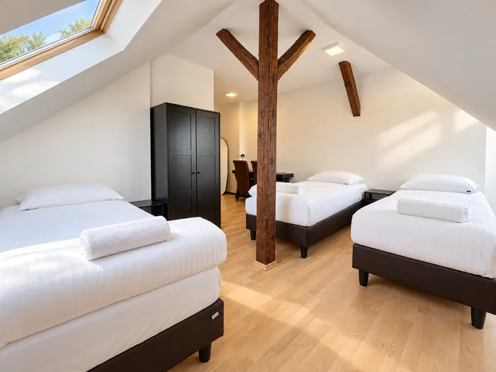 Dachzimmer mit Holzbalken, Dachfenster und drei Betten